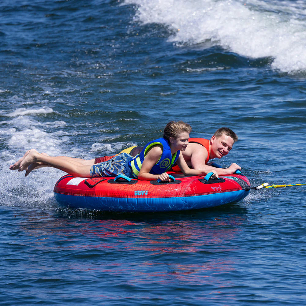 Two children on a red and blue inflatable tube in the water.